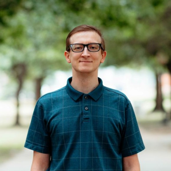 Man dressed nicely smiling at the camera with trees behind him