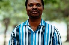Man dressed nicely smiling at the camera with trees behind him