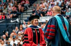 Woman wearing academic regalia smiling in front of crowd