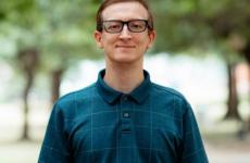 Man dressed nicely smiling at the camera with trees behind him