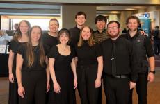 9 students dressed nicely in dark colors standing and smiling at the camera