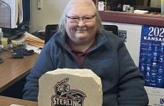 Woman wearing eyeglasses smiling at camera with a Sterling College Warrior logo in front of her