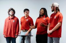 Four students wearing matching red shirts and making a presentation