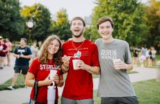 Three students smiling standing in front of trees and holding cups of ice cream