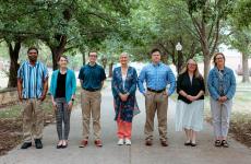Seven people dressed nicely and standing on a sidewalk with trees behind them
