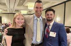 3 people dressed nicely standing in a ballroom smiling for the camera