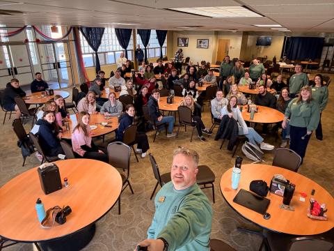 Man takes selfie of the whole room of students and teachers sitting in chairs