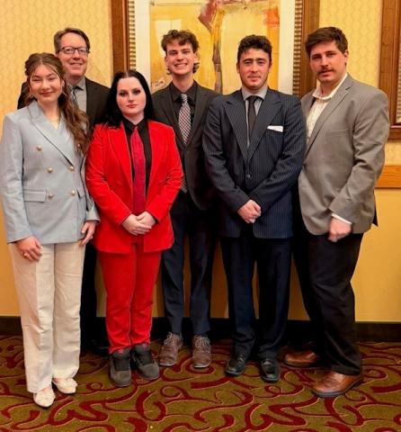 6 people standing dressed nicely and smiling at the camera