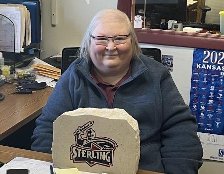 Woman wearing eyeglasses smiling at camera with a Sterling College Warrior logo in front of her