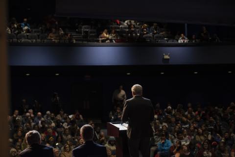 Auditorium of people with speaker facing the crowd from the stage