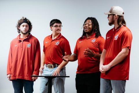 Four students wearing matching red shirts and making a presentation