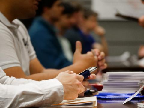 Close up shot of people lined up to talk to someone else on the other side of a table