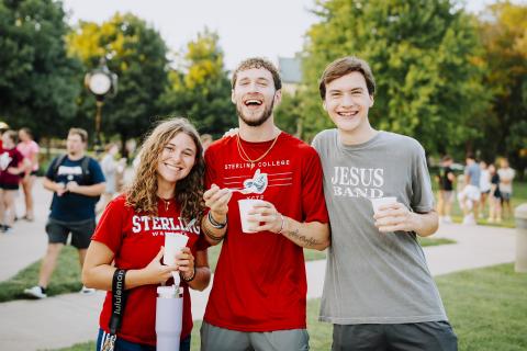 Three students smiling standing in front of trees and holding cups of ice cream