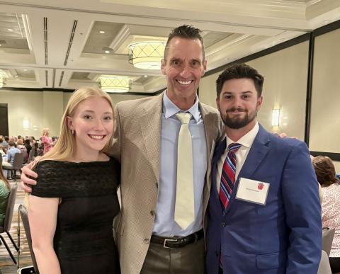 3 people dressed nicely standing in a ballroom smiling for the camera