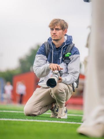 Man kneeling on field holding a camera Man kneeling on field holding a camera