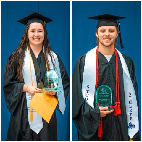 two students wearing graduation attire and holding glass awards