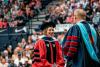 Woman wearing academic regalia smiling in front of crowd