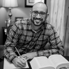 Man writing on paper with a book in front of him smiling and looking at the camera