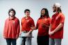 Four students wearing matching red shirts and making a presentation